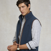 Man wearing a blue gilet over a plaid shirt on a neutral background